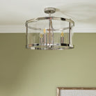 Semi-flush chrome ceiling light with clear glass and warm glowing bulbs, on a green ceiling.