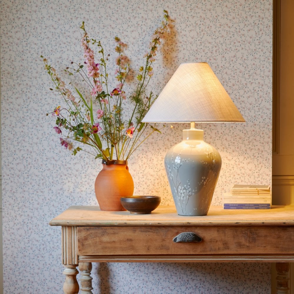A white tapered lampshade on a grey base with a terra cotta vase of flowers.