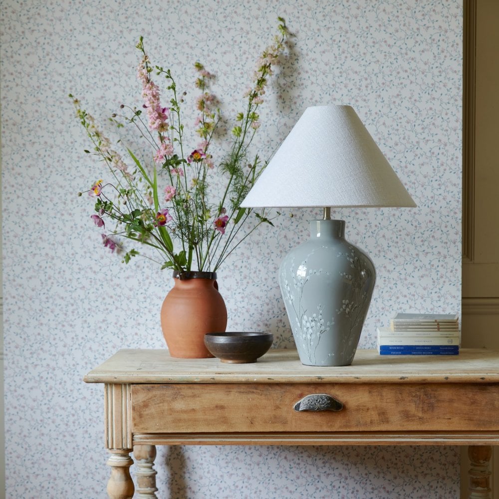 A white tapered lampshade on a grey base with a terra cotta vase of flowers.