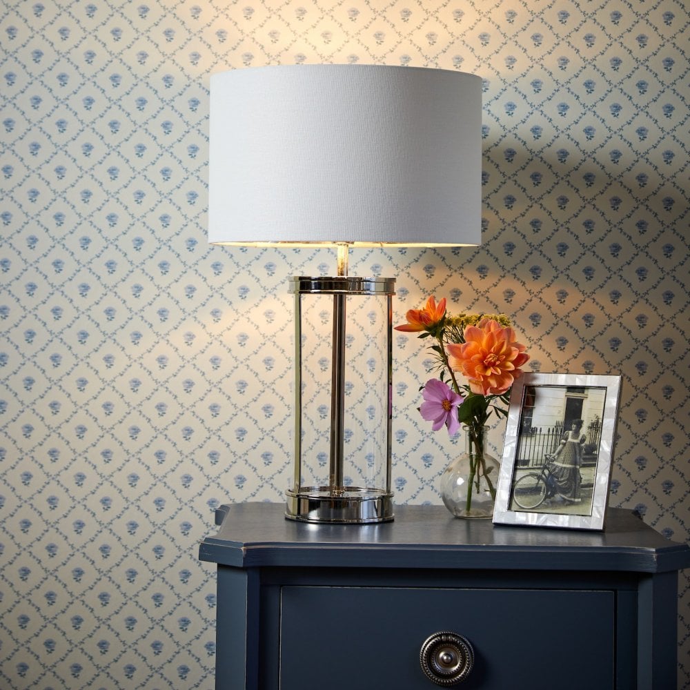 A modern lamp on a blue bedside table, with flowers and a picture frame.