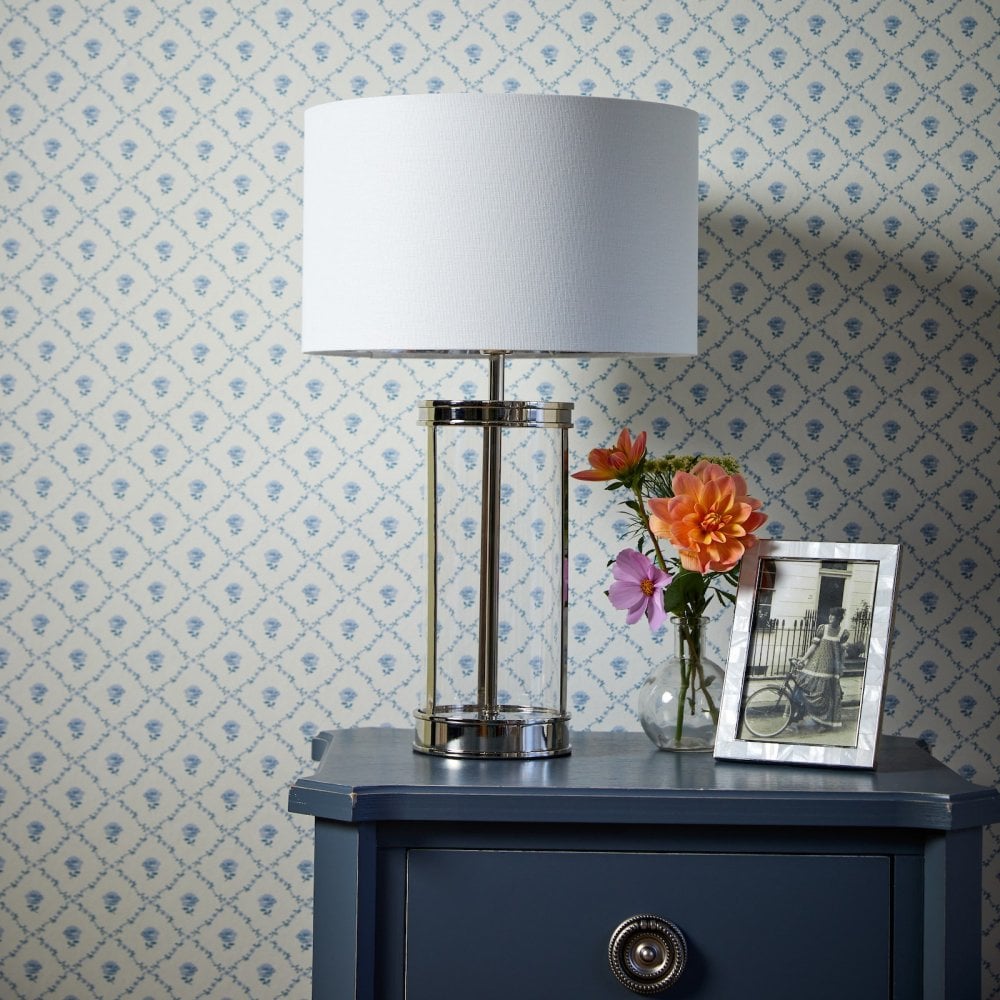 A modern lamp on a blue bedside table, with flowers and a picture frame.