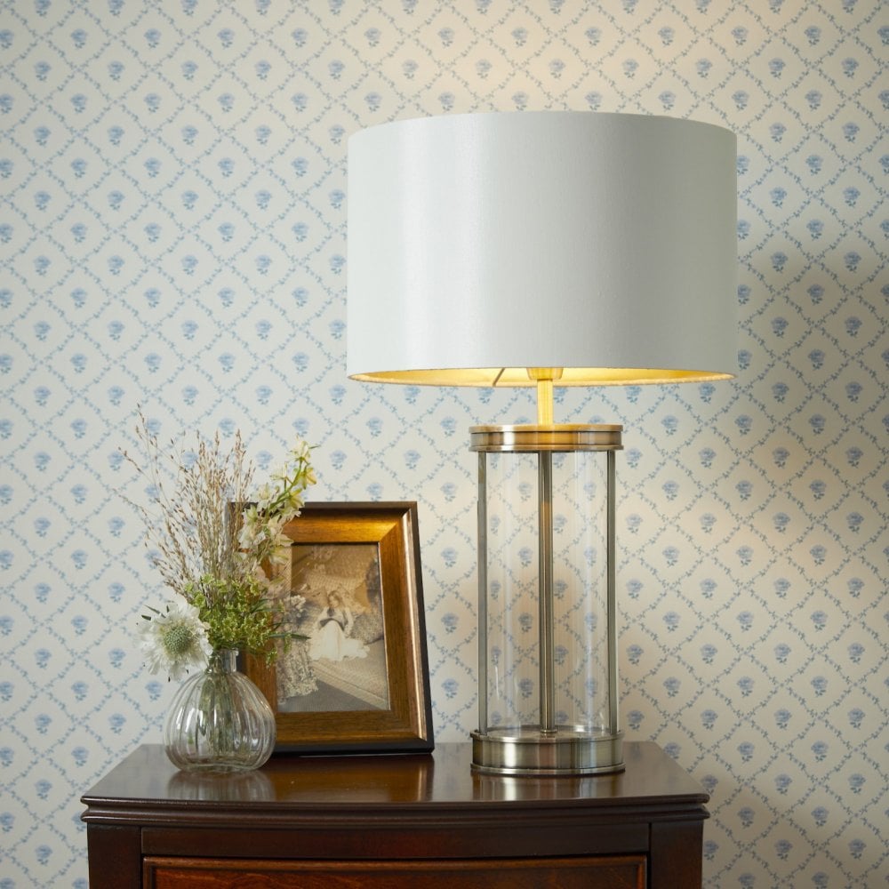 A white lampshade with a glass and gold base is on a dark wood table.
