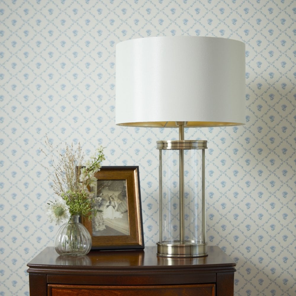 A white lampshade with a glass and gold base is on a dark wood table.