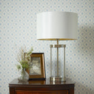 A white lampshade with a glass and gold base is on a dark wood table.