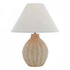 A studio shot of a wicker table lamp with a conical off-white shade.