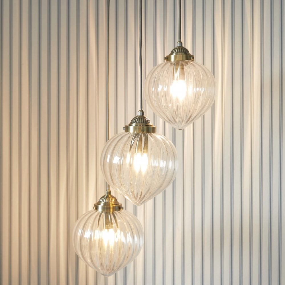 Three ribbed glass pendant lights with brass fittings hang against a striped wall.