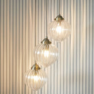 Three ribbed glass pendant lights with brass fittings hang against a striped wall.