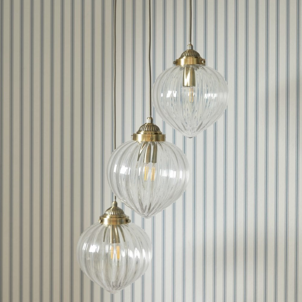 Three ribbed glass pendant lights with brass fittings hang against a blue and white striped wall.