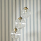 Three ribbed glass pendant lights with brass fittings hang against a blue and white striped wall.