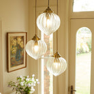 Three ribbed glass pendant lights with brass fittings illuminate a bright room.