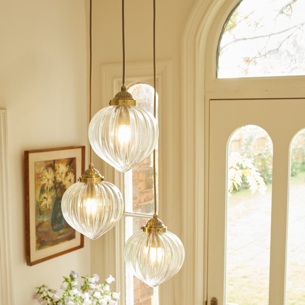 Three ribbed glass pendant lights with brass fittings hang by a large window.