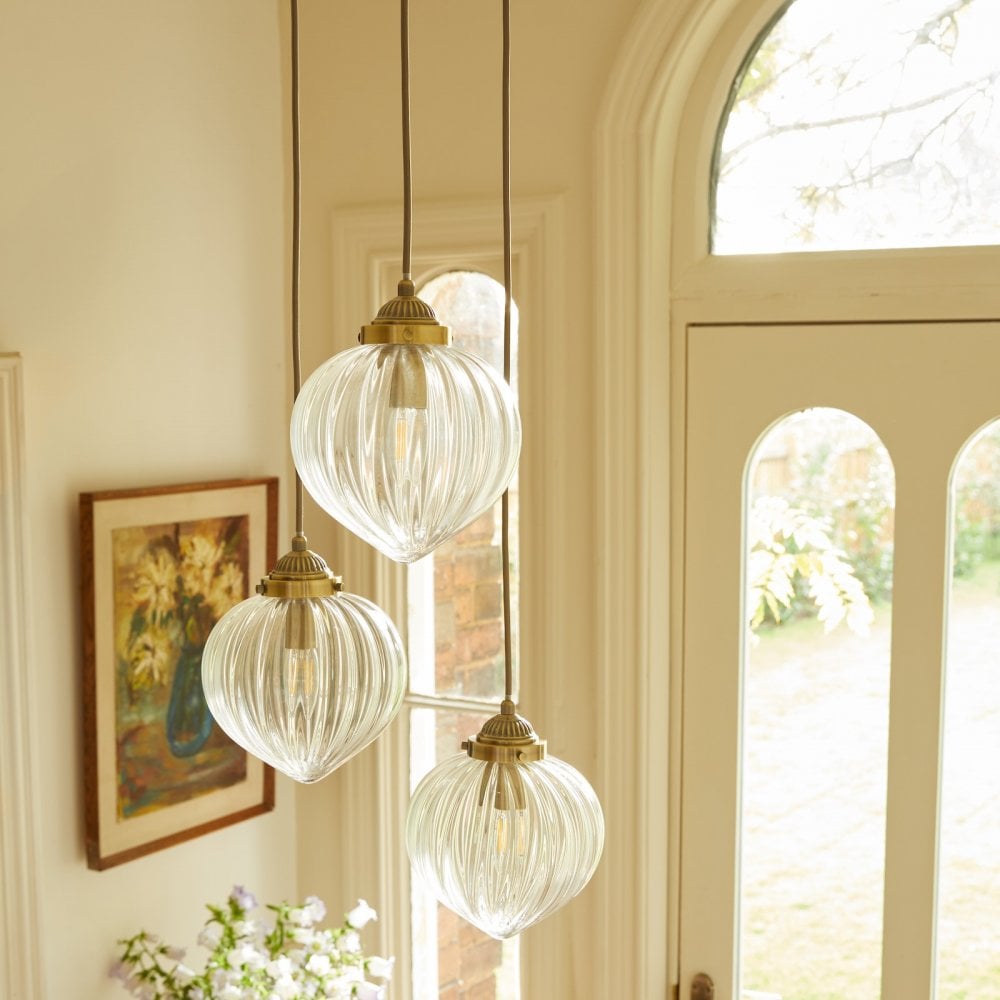 Three ribbed glass pendant lights with brass fittings hang next to a window and artwork.