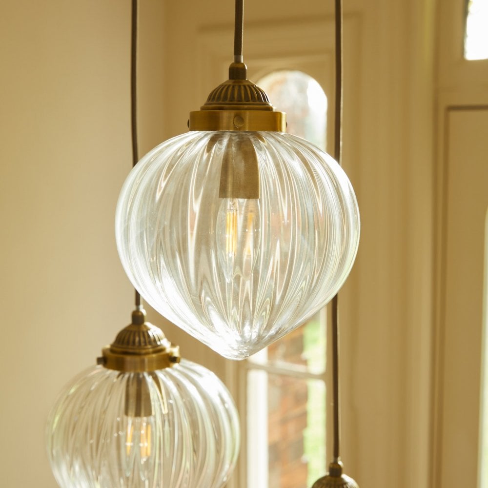Detailed view of a ribbed glass pendant light with a brass fitting and illuminated bulb.