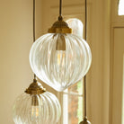 Detailed view of a ribbed glass pendant light with a brass fitting and illuminated bulb.