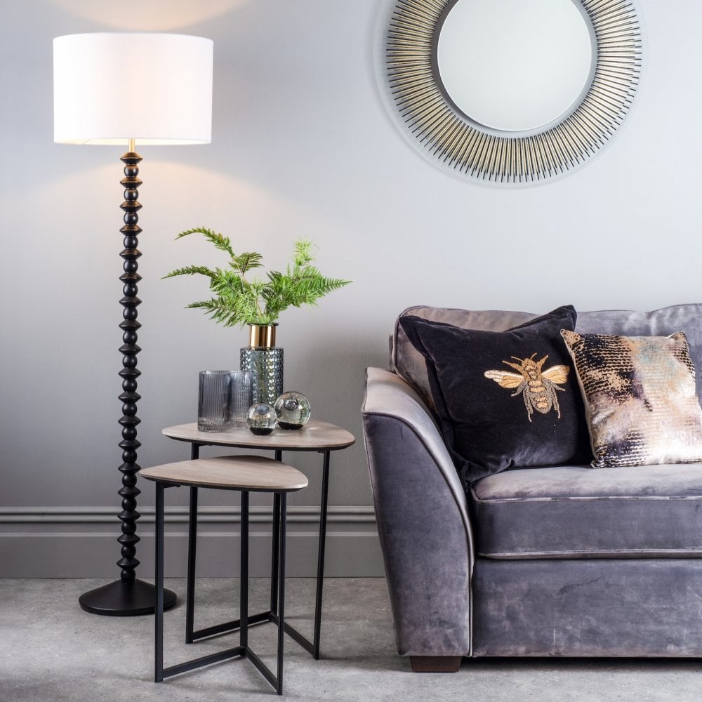 Black textured floor lamp illuminating a contemporary living room with a gray sofa and mirror.