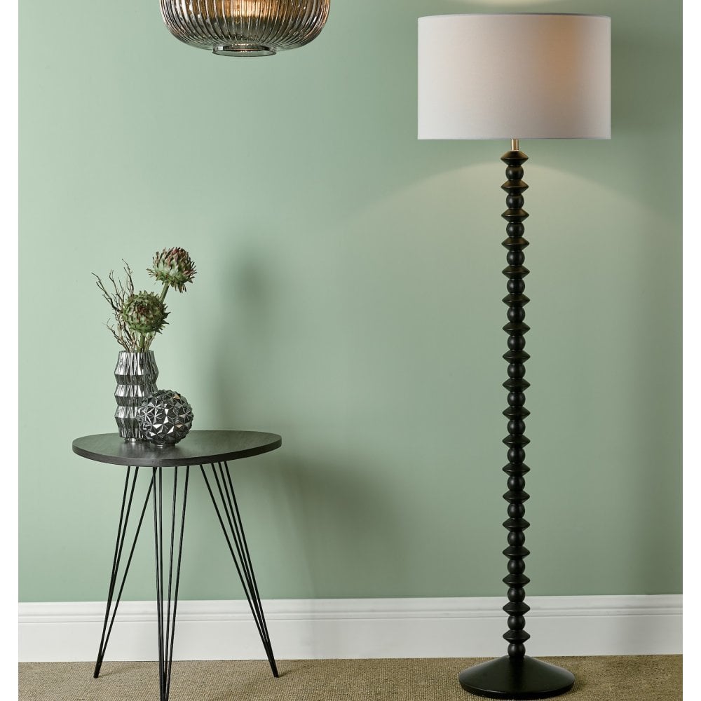 Tall black textured floor lamp beside a small round table with a vase, against a green wall.