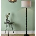 Tall black textured floor lamp beside a small round table with a vase, against a green wall.