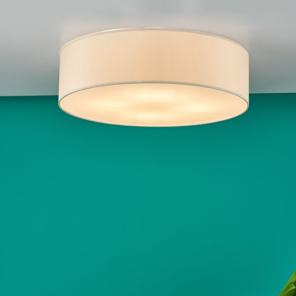 A round, cream-colored fabric ceiling light installed on a white ceiling above a teal wall.