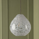 Teardrop pendant light with white and clear speckled glass against a green panelled wall.