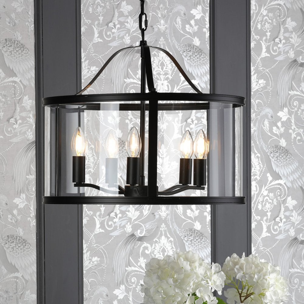 A black chandelier with clear glass panels, illuminating a patterned wall and a floral arrangement.