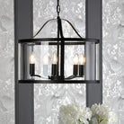 A black chandelier with clear glass panels, illuminating a patterned wall and a floral arrangement.