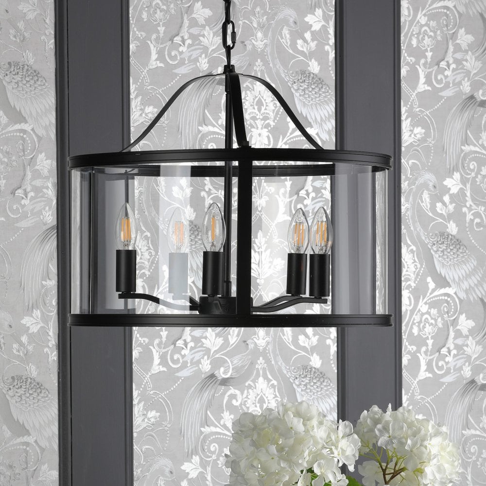 A black chandelier with clear glass, casting a warm glow over a patterned wall and white flowers.
