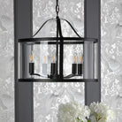 A black chandelier with clear glass, casting a warm glow over a patterned wall and white flowers.