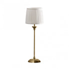 A brass table lamp with a pleated white shade against a white background.