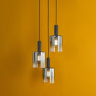A modern chandelier featuring three glass cylindrical shades hanging against an orange wall.