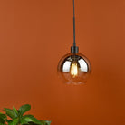 A contemporary smoked glass pendant light, casting a warm glow on an orange wall.