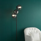 A floor lamp with three spherical smoked glass shades next to a white armchair in a green room.
