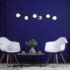 Modern black chandelier with white lightbulbs over a coffee table and white chairs.