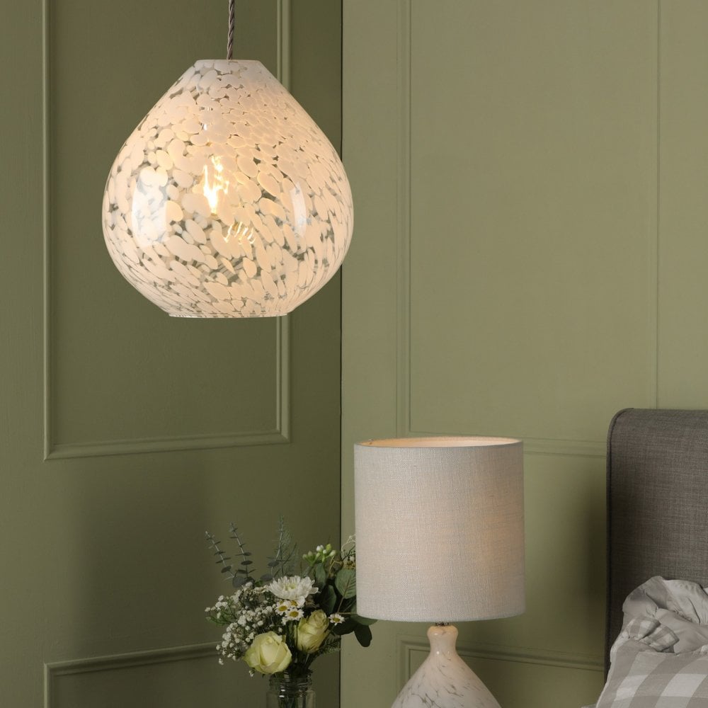 Teardrop pendant light hanging in a bedroom above a bedside table lamp and flowers.
