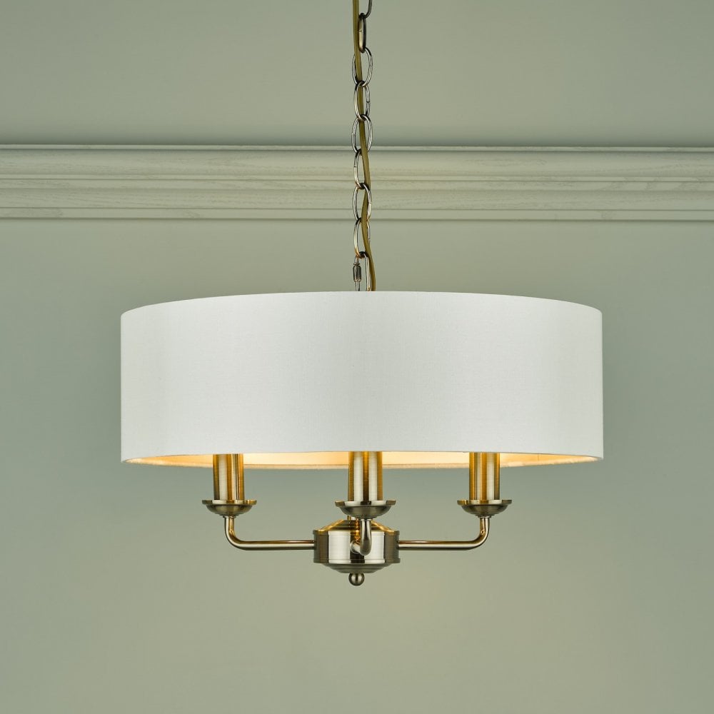 A brass three-arm pendant light with a white drum shade against a light green wall.