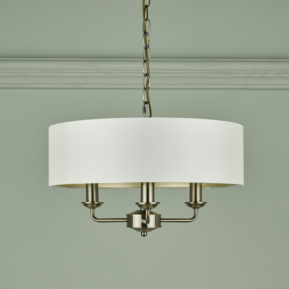 A brass three-arm pendant light with a white drum shade against a light green wall.