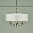 A brass three-arm pendant light with a white drum shade against a light green wall.