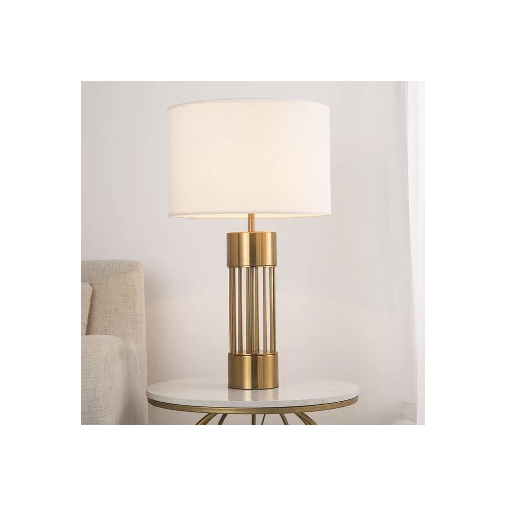 A stylish table lamp with a white shade and a gold base on a marble side table.