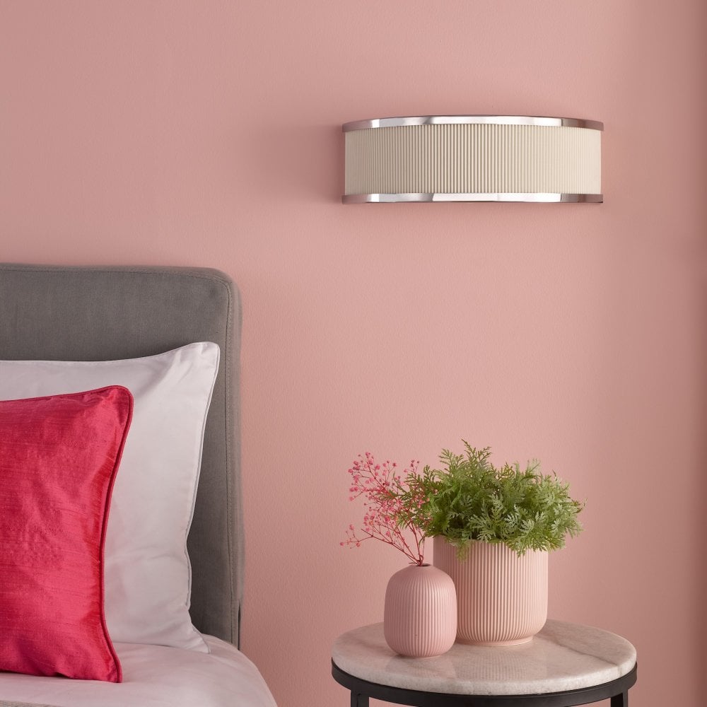 A wall sconce provides soft lighting above a bedside table in a blush pink room.