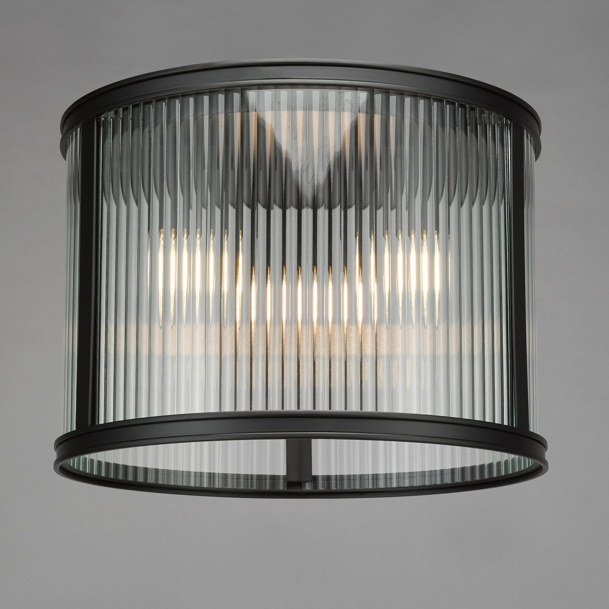A close up view of a ceiling mounted cylindrical light with fluted glass and a black frame.