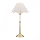 A brass table lamp with a cream scalloped shade on a white background.
