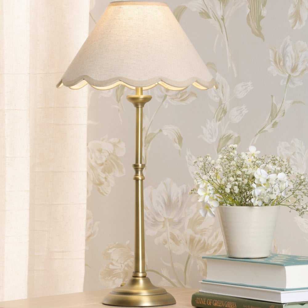 A lit brass table lamp with a scalloped cream shade on a wooden surface.