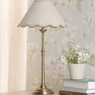 A brass table lamp with a scalloped cream shade, next to a vase of white flowers.