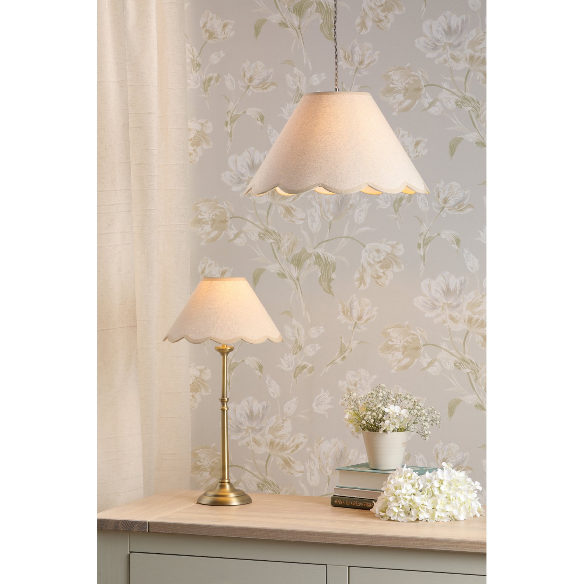 A brass table lamp and a pendant light, both with scalloped cream shades, in a room.