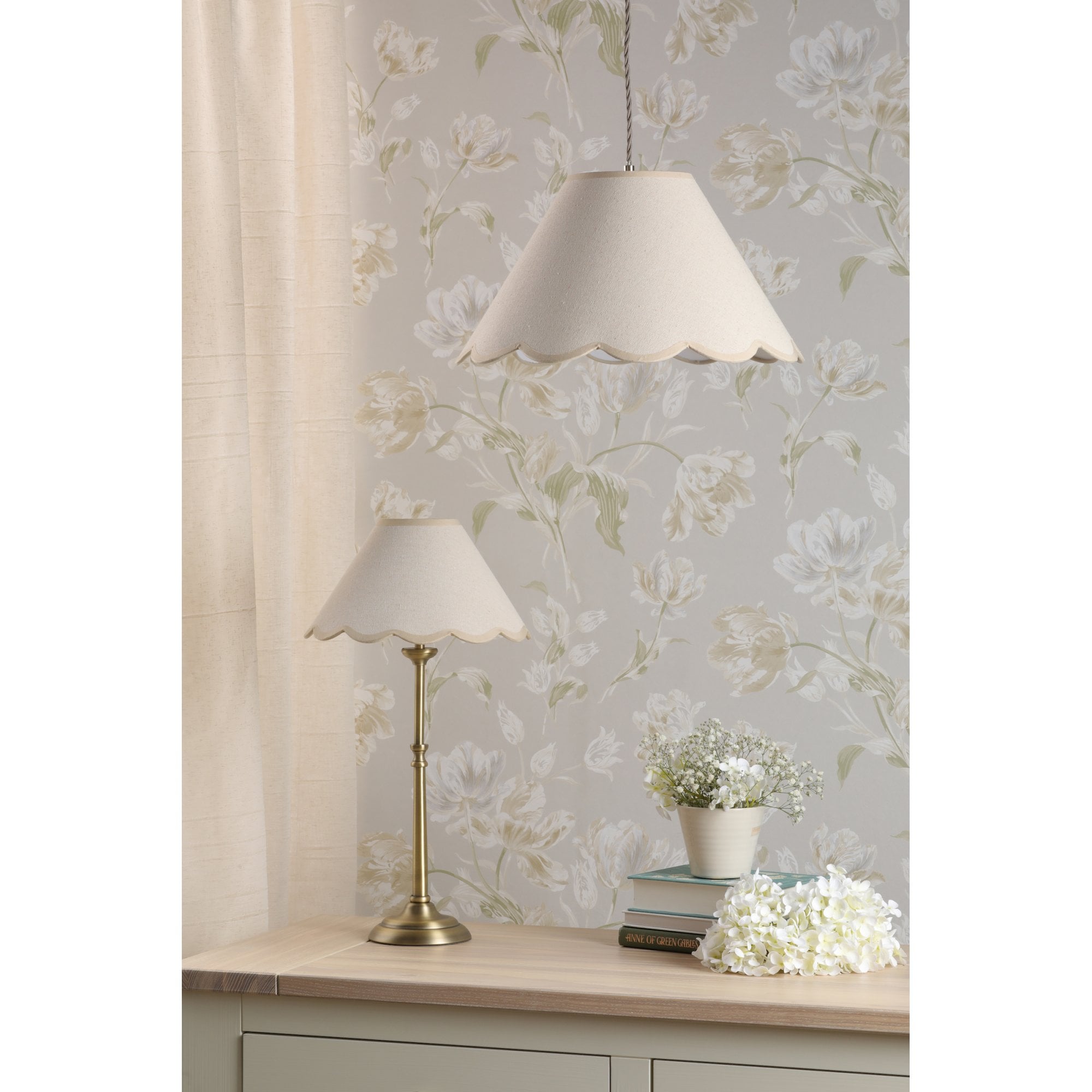 A brass table lamp and a pendant light with scalloped cream shades in a room setting.