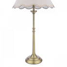 Close-up of the base and stem of a brass table lamp with a cream scalloped shade.