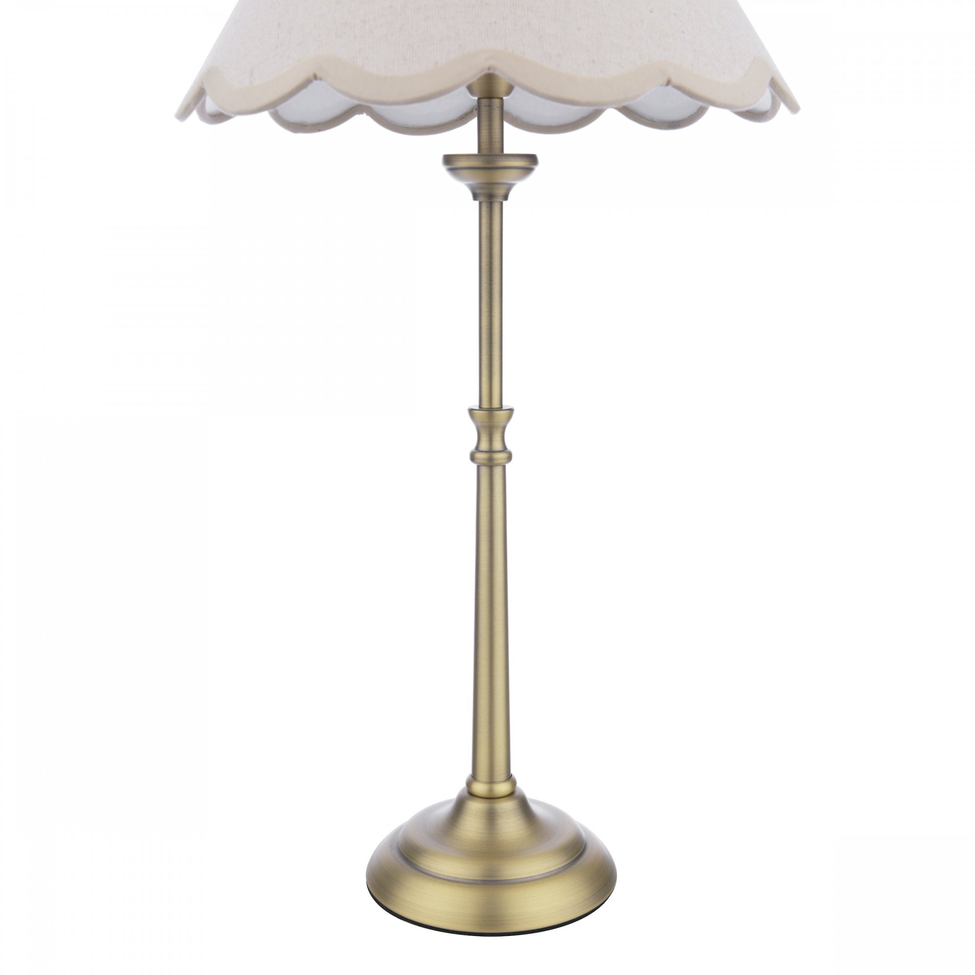 Close-up of the base and stem of a brass table lamp with a cream scalloped shade.