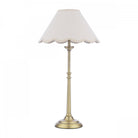 A brass table lamp with a cream scalloped shade on a white background.