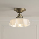 A brass ceiling light with a translucent ruffled glass shade, illuminating a soft glow.