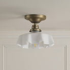 A brass ceiling light with a ruffled, translucent glass shade on a light ceiling.