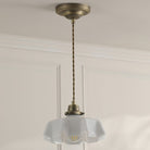 A brass pendant light with a white fluted glass shade hangs from a ceiling.